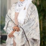 Woman wearing a Simar Lace Parsha Abaya in a soft gray pattern with elegant black lace details, styled with a white hijab.